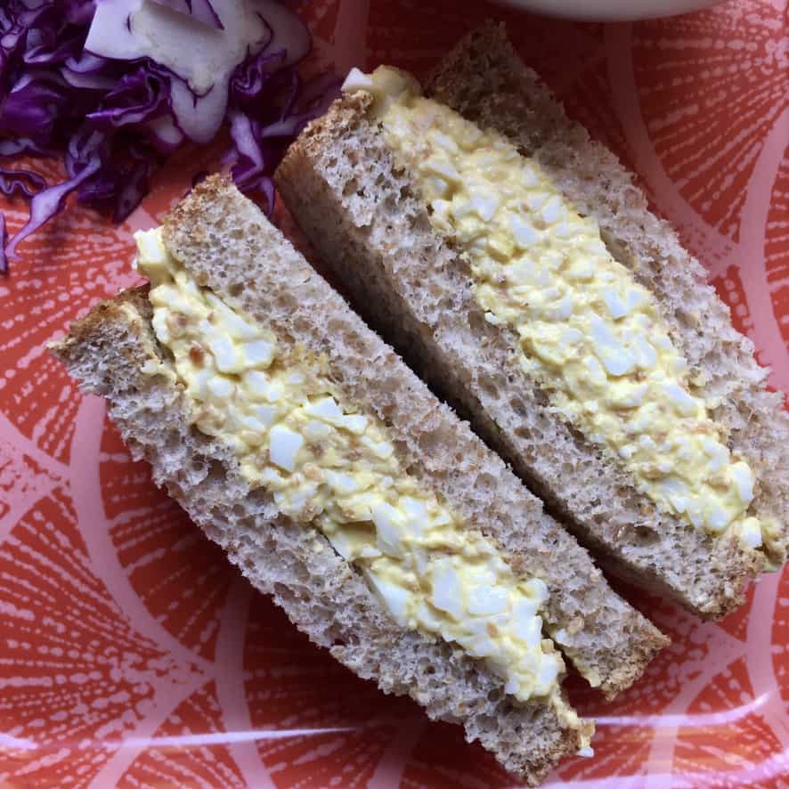 sesame egg salad sandwich sliced with the middles facing out and up lying on a coral and pink colored Japanese inspired tray with shaved purple cabbage barely in view