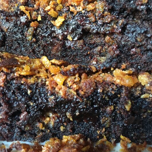 a stack of two brownies on top of each other with a layer of golden brown cornflake crunch on the top of each one