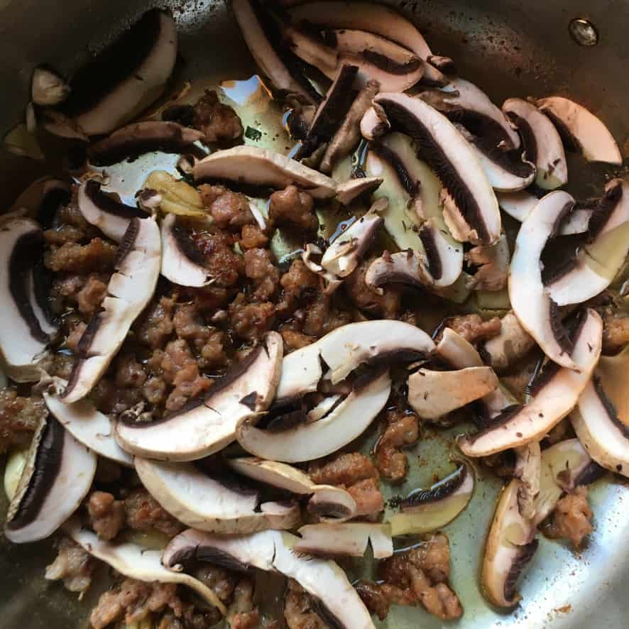 sausage browned in a stainless steel pan with garlic and olive oil with fresh sliced button mushrooms added