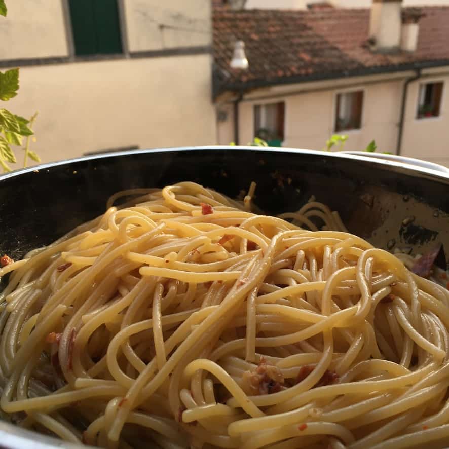 pan full of spaghetti con aglio e olio con prosciutto fritto with a view out of the window in Italy