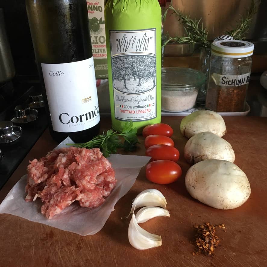 raw ingredients for the mussels recipe on a cutting board including white wine, EVOO, sausage, mushrooms, garlic, tomatoes, crushed red peppers