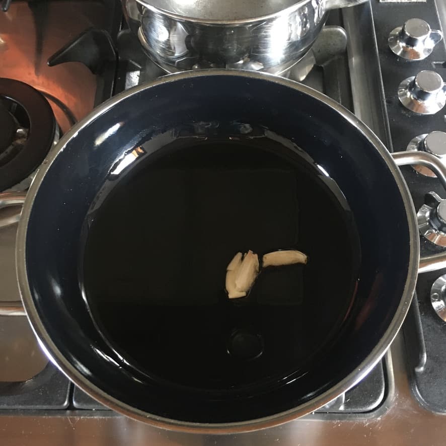 Garlic clove being fried in olive oil to turn it into a garlic paste for spinach and ricotta ravioli filling with extra flavor (that's not overwhelming or even noticeably garlic-flavored.