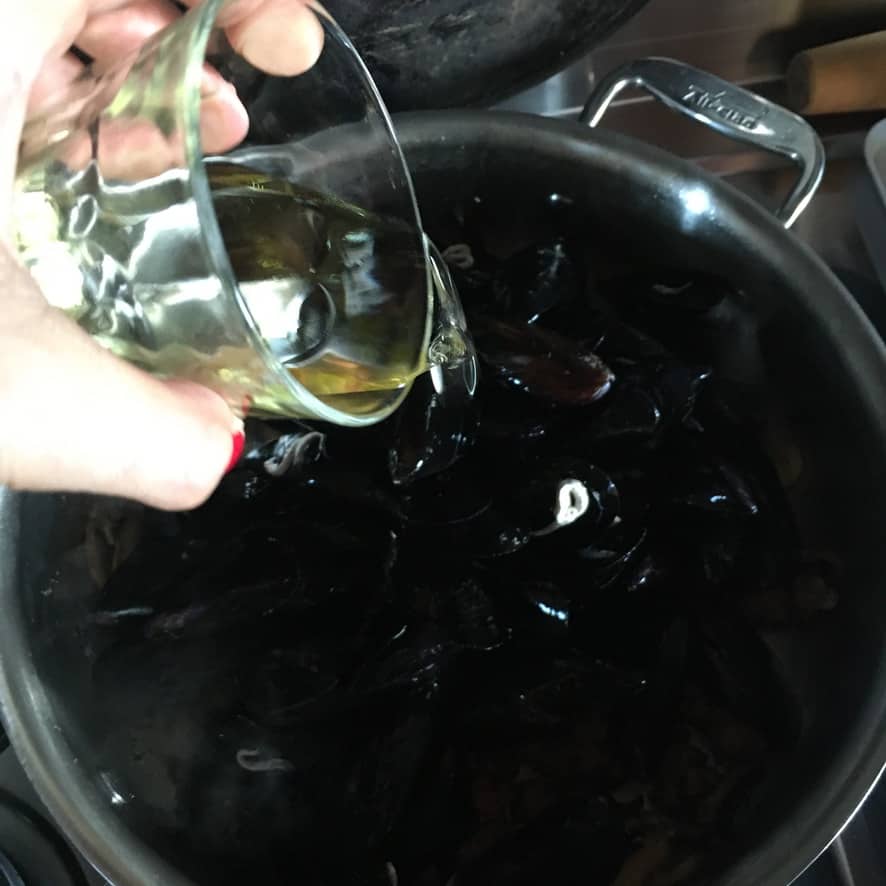 pouring white wine into the pot with mussels
