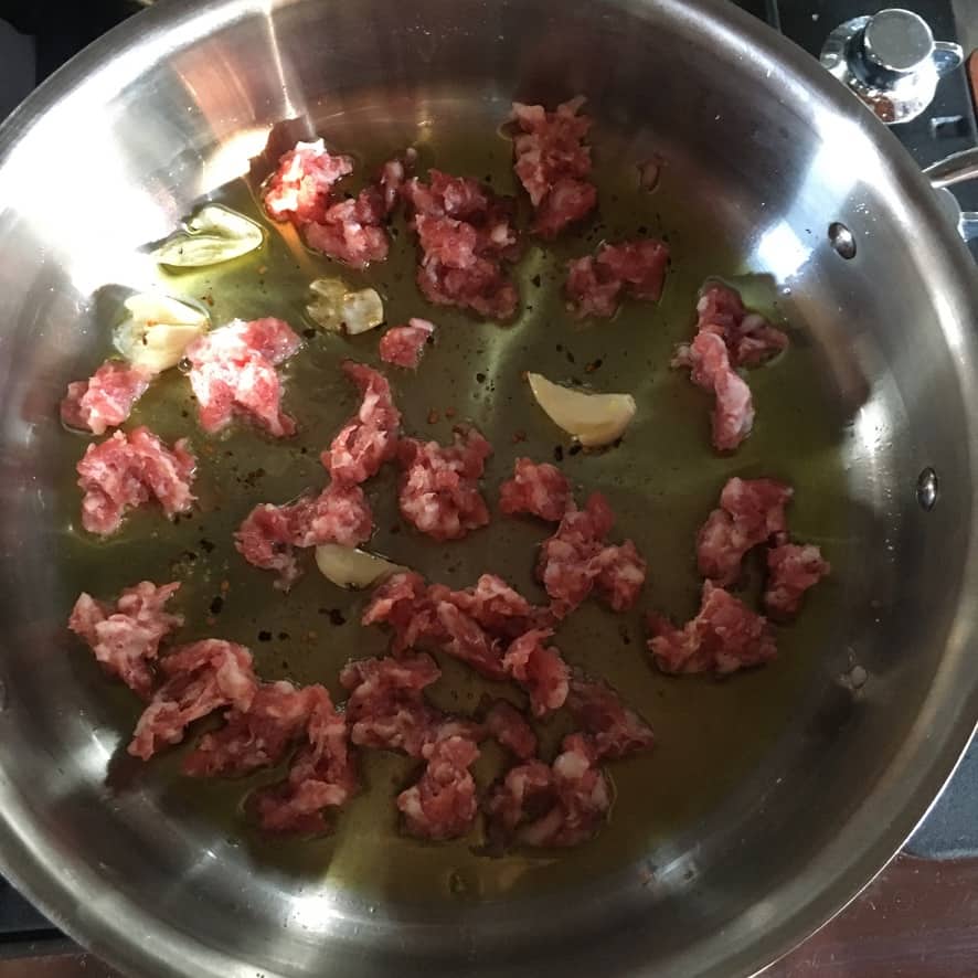 raw pork sausage just added to the pan with EVOO and garlic cloves