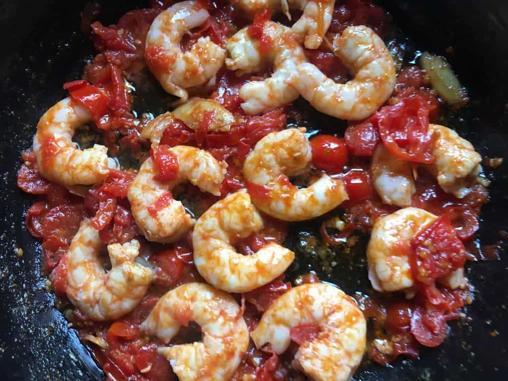 cooked slightly coral colored shrimp in a tomato and olive oil sauce in a dark Silit Brand braising pan