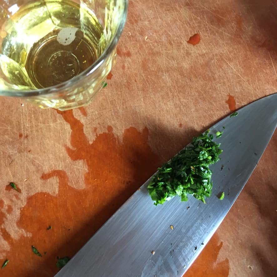 chopped parsley on a knife blade on a cutting board
