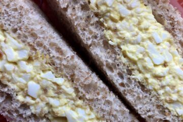 closeup of sesame egg salad on whole wheat bread that's been cut into triangles and the middles facing out and up towards you