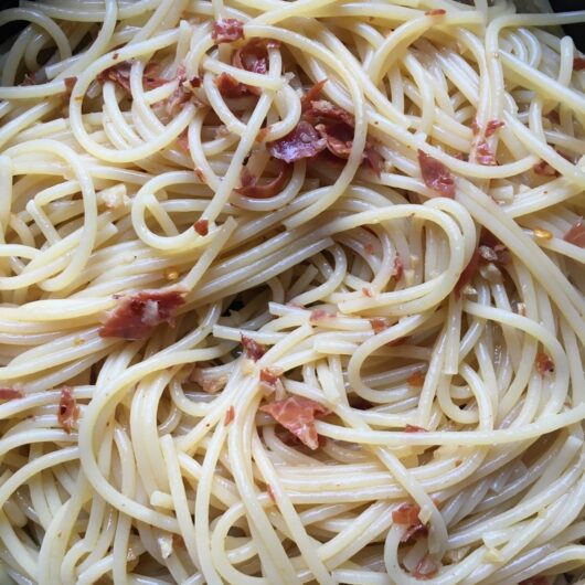 pan full of perfectly cooked pasta with bits of garlic and crispy prosciutto