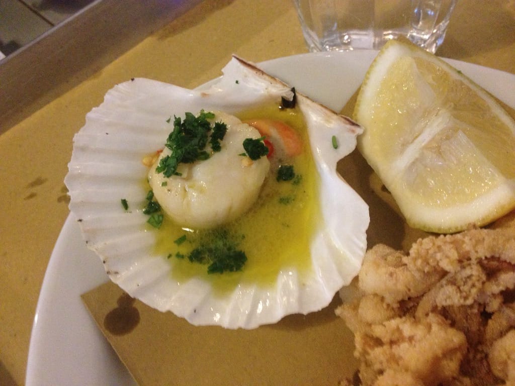grilled scallops in butter and olive oil with parsley on top next to a lemon wedge and calamari