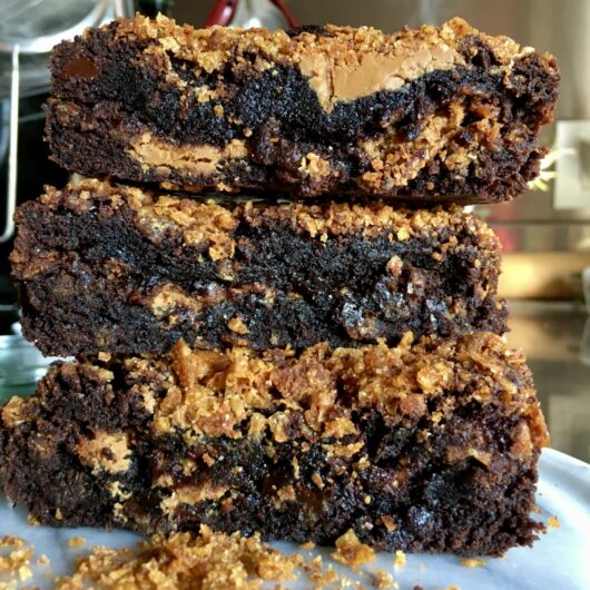 closeup of a stack of brownies with very moist and glistening chocolatey fudgey centers and Biscoff spread with crispy cornflake crunch on top and scattered on the serving platter