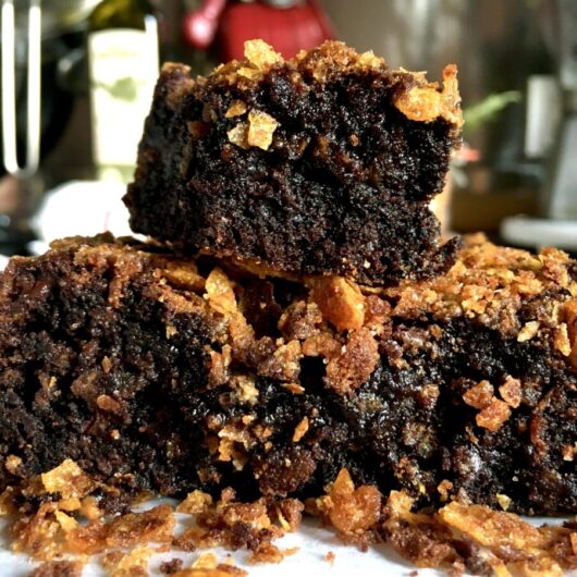 closeup of a stack of brownies with very moist and glistening chocolatey fudgey centers and Biscoff spread with crispy cornflake crunch on top and scattered on the serving platter