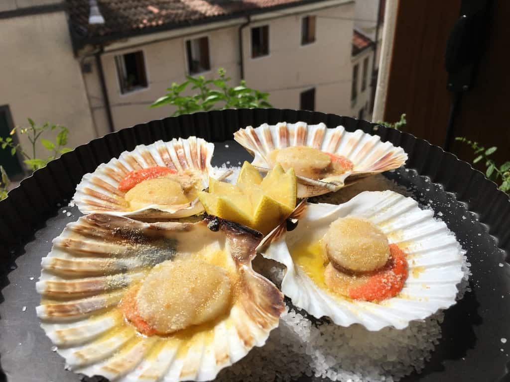 4 3 raw scallops in the shell sprinkled with bread crumbs and extra virgin olive oil with a view of the italian homes in the background out of the window