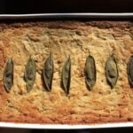 beautifully golden brown cornbread dressing with 7 sage leaves in a line in the middle