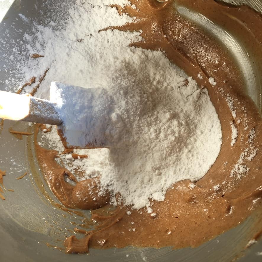 glossy peanut butter and butter mixture in a bowl with spatula with powdered sugar added to the bowl