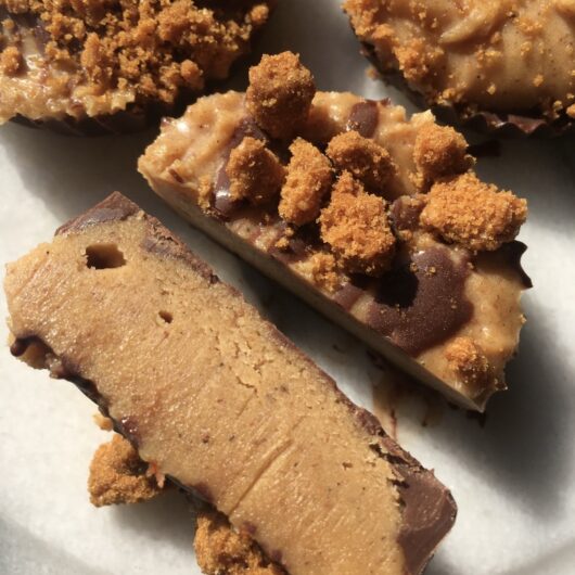closeup of a cut peanut butter cup revealing the thick inner peanut butter layer speckled with vanilla beans and dotted with crumbled Biscoff cookies