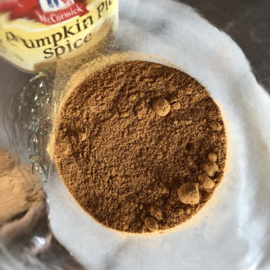 a view down into a glass Weck jar filled with homemade pumpkin pie spice blend with a McCormick's container in view through the glass