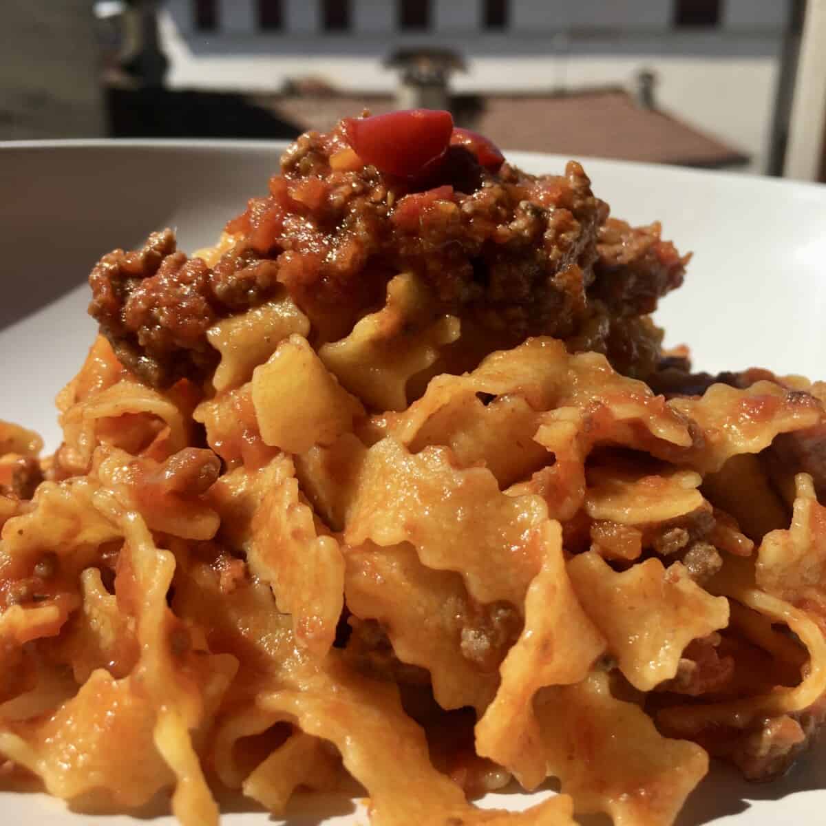 a bowl full of Reginelle tagliatelle pasta which is a tagliatelle egg pasta with zigzagged edges (with a beautiful beef ragù mixed in) with a view of the Italian homes and blue sky in the background