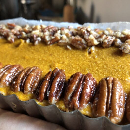 pumpkin pie filling added to biscoff cookie crust in rectangular tart pan with removable bottom smoothed out and decorated with pecans