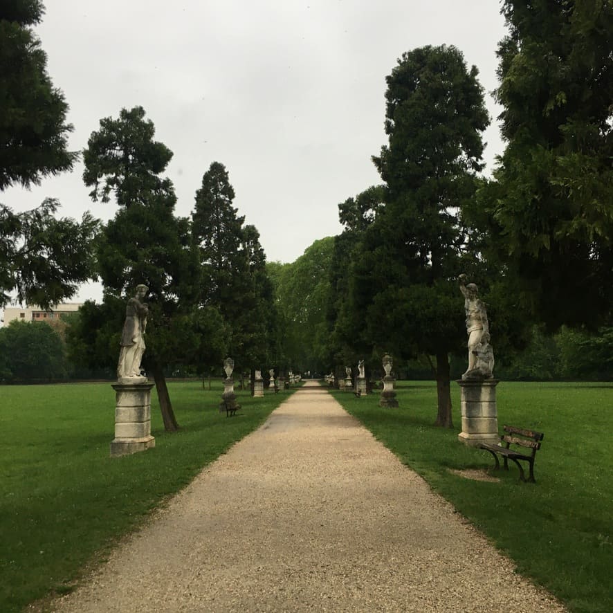 a view of ancient sculptures of people lining a walkway in the park with trees also lining the path
