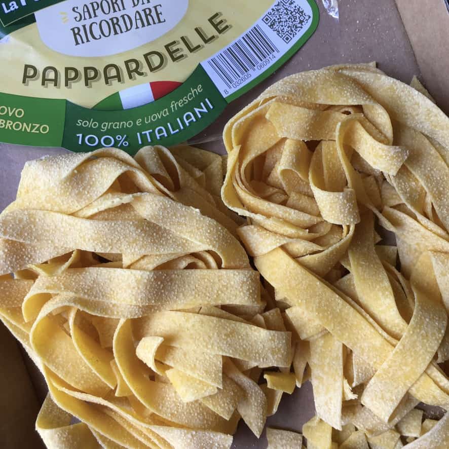 dried pappardelle pasta nests next to each other with the package visible in the background