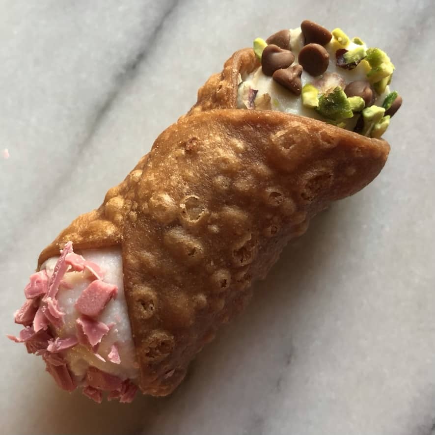 a beautiful golden brown cannoli with pink strawberry ricotta cream