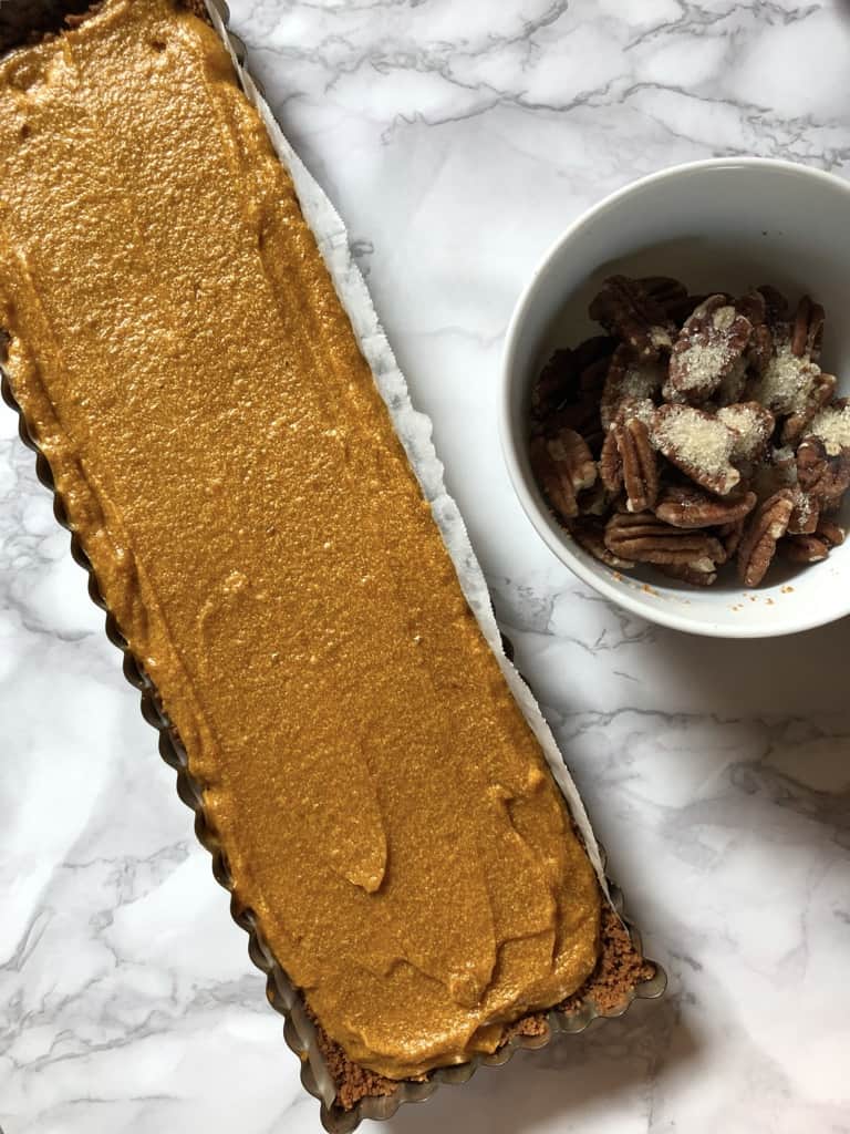 pumpkin pie filling added to biscoff cookie crust in rectangular tart pan with removable bottom smoothed out and ready to decorate with pecans