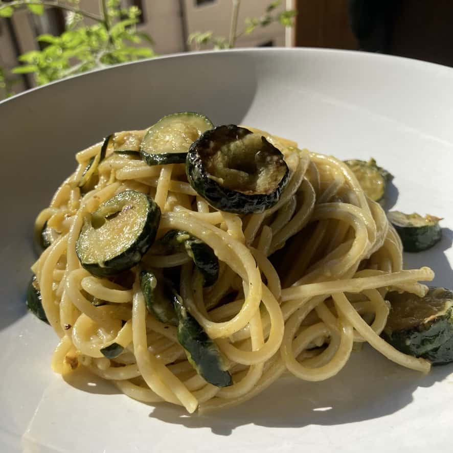 spaghetti with zucchini in a white pasta bowl with Italian homes in the background in the view out of the window