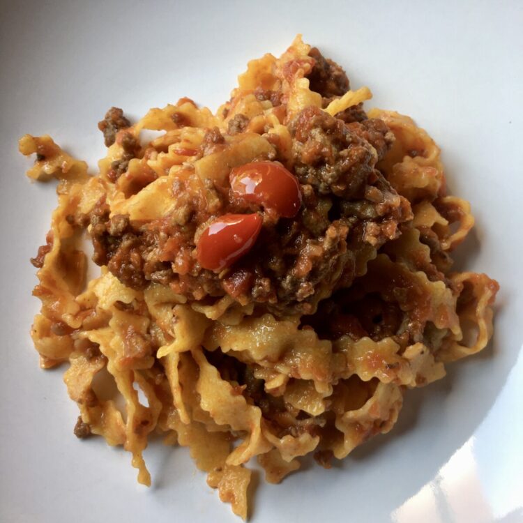 a bowl full of Reginelle tagliatelle pasta which is a tagliatelle egg pasta with zigzagged edges (with a beautiful beef ragù mixed in)