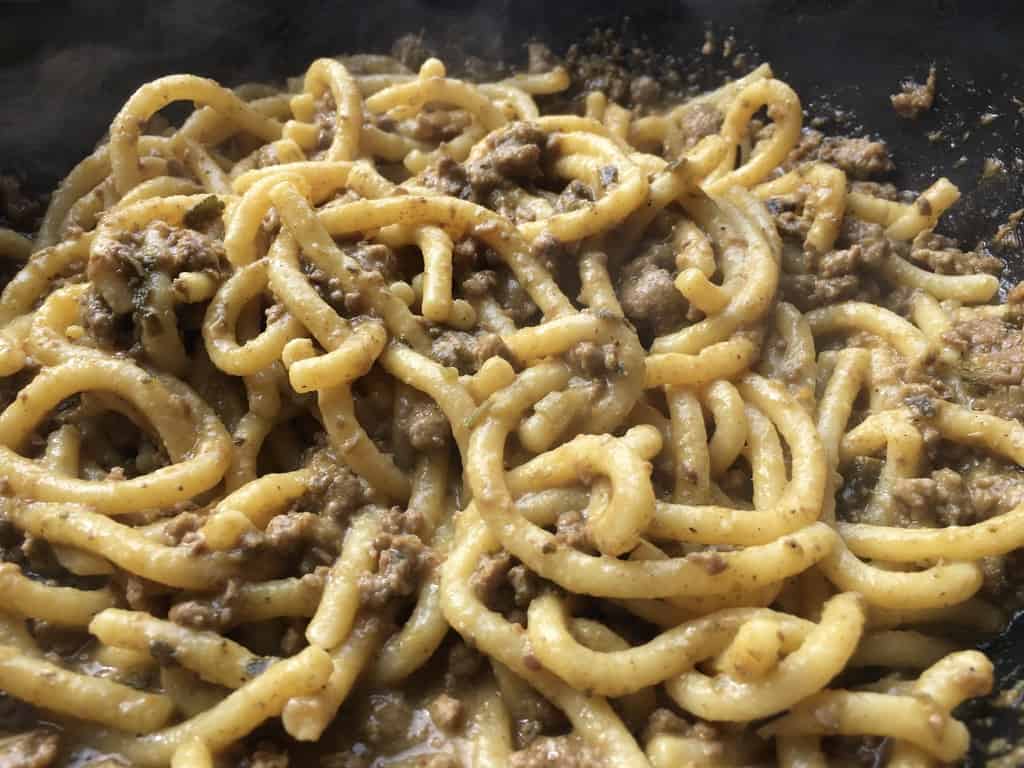 A braising dish filled with fat bigoli egg pasta noodles covered in duck ragù