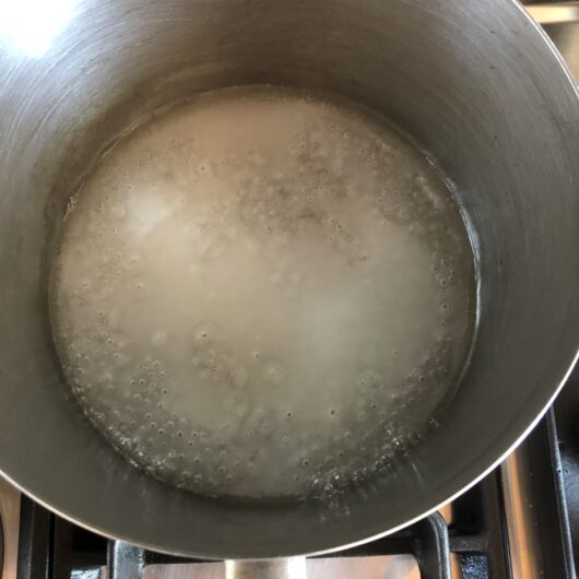 sugar and water added to a pot and the heat turned up to high to cook it with the first bubbles starting to happen