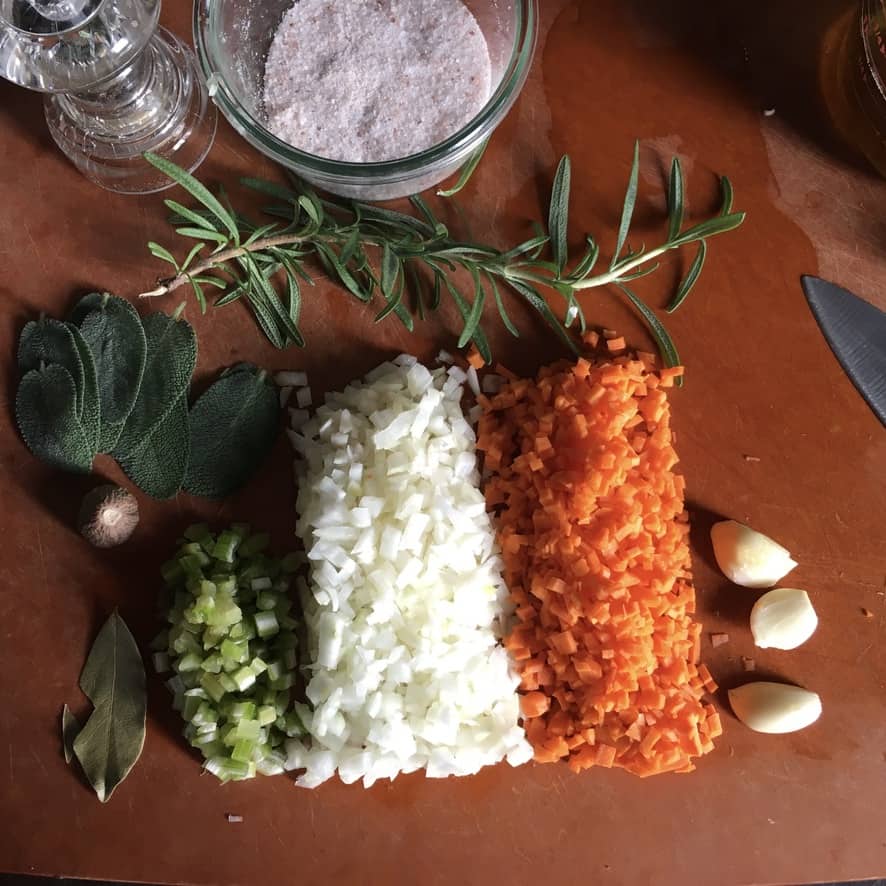 soffritto and herbs plus salt and pepper mill on a cutting board