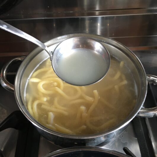 a ladle full of starchy cooking water above the pot with cooking bigoli pasta