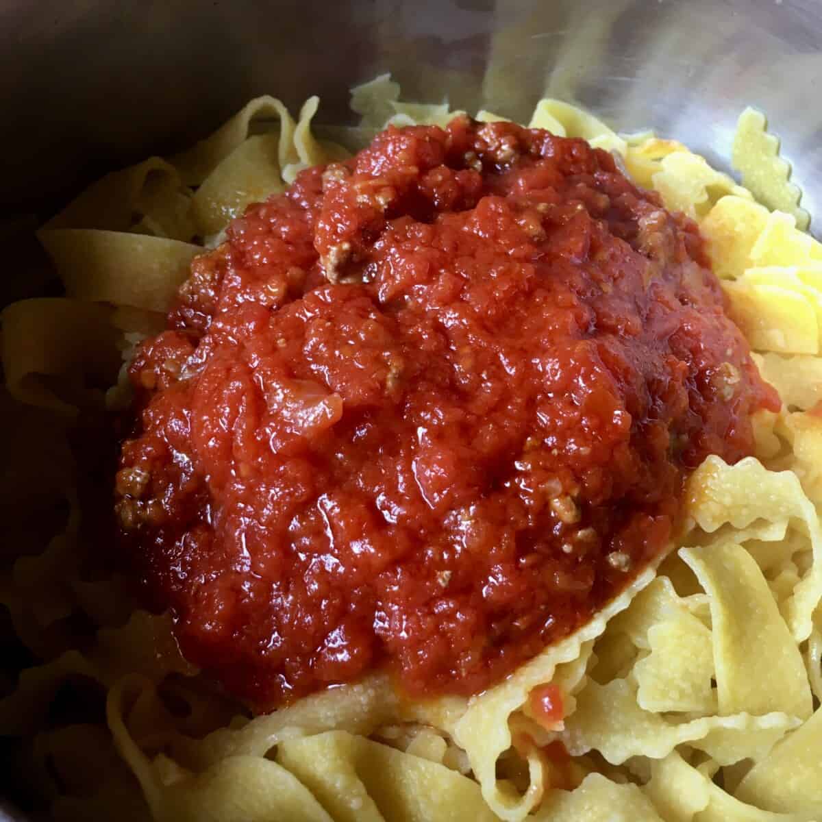 a pot full of Reginelle tagliatelle pasta which is a tagliatelle egg pasta with zigzagged edges (with a beautiful simple beef ragù (cooked less than the classic ragù an much brighter red) mixed in)