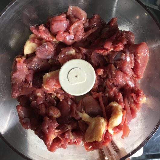 raw chunks of duck meat in the bowl of a food processor