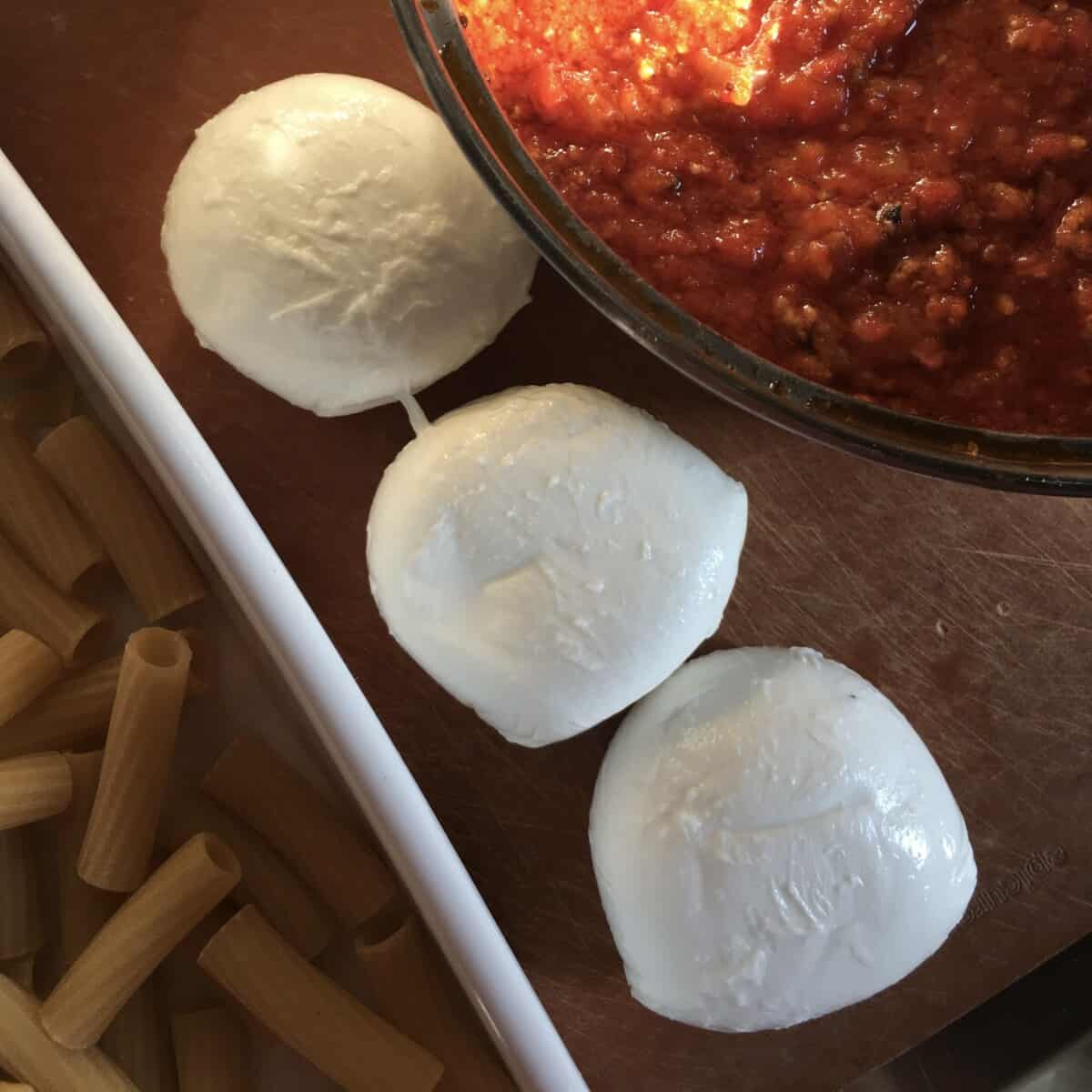 3 fresh balls of mozzarella in between pasta and pasta sauce on a cutting board