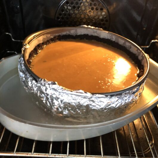 caramel-colored cheesecake batter in a springform pan about to be baked in a water bath