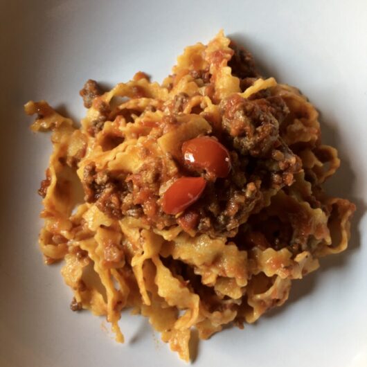 a bowl full of Reginelle tagliatelle pasta which is a tagliatelle egg pasta with zigzagged edges (with a beautiful beef ragù mixed in)