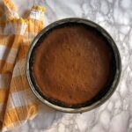 baked darker colored caramel-colored cheesecake in a springform pan after baking and cooling and no longer puffy