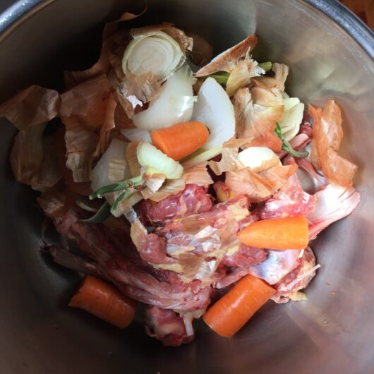 a pressure cooker filled with duck stock ingredients including carrots, onion, celery, duck bones and scraps