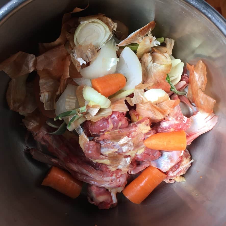 Apressure cooker filled with duck stock ingredients including carrots, onion, celery, duck bones and scraps.