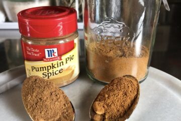 pumpkin pie spice on two spoons (one spoon has McCormick's brand pumpkin pie spice and the other is my homemade spice blend with a small bottle of McCormick's in the background and also a small Weck hermetic jar containing my homemade pumpkin spice each behind their respective spoons