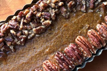 Pumpkin mascarpone tart topped with pecans on a cutting board.