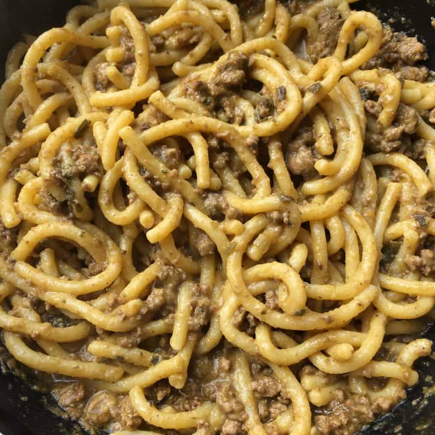 A braising dish filled with fat bigoli egg pasta noodles covered in duck ragù