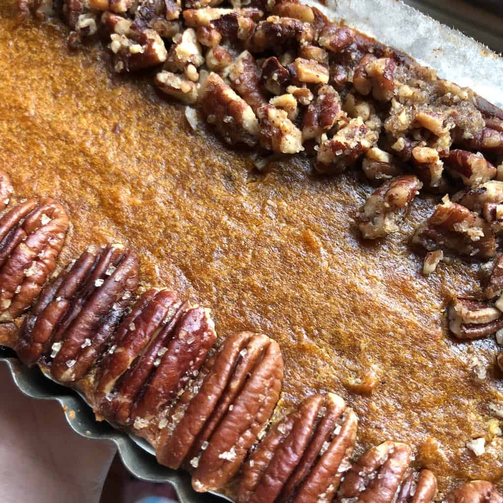 All-natural Pumpkin mascarpone Pie with Pecan Crunch in a rectangular tart pan on a cutting board.