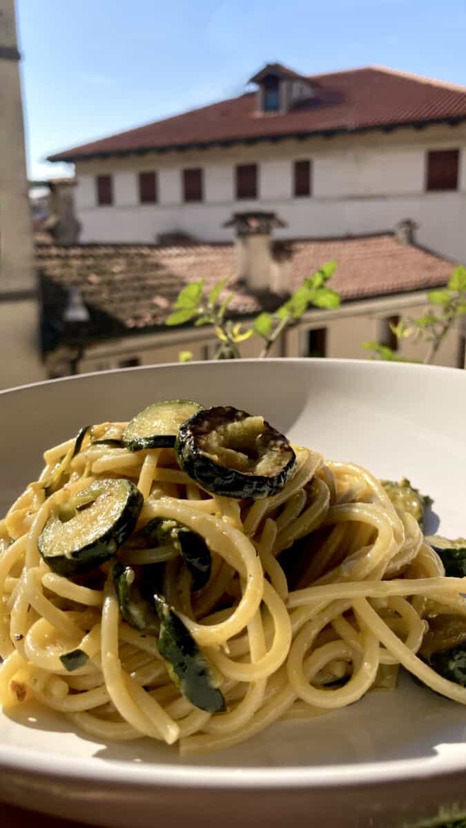 a bowl of spaghetti alla zucchini with a view out of the window with Italian rooftops in the background