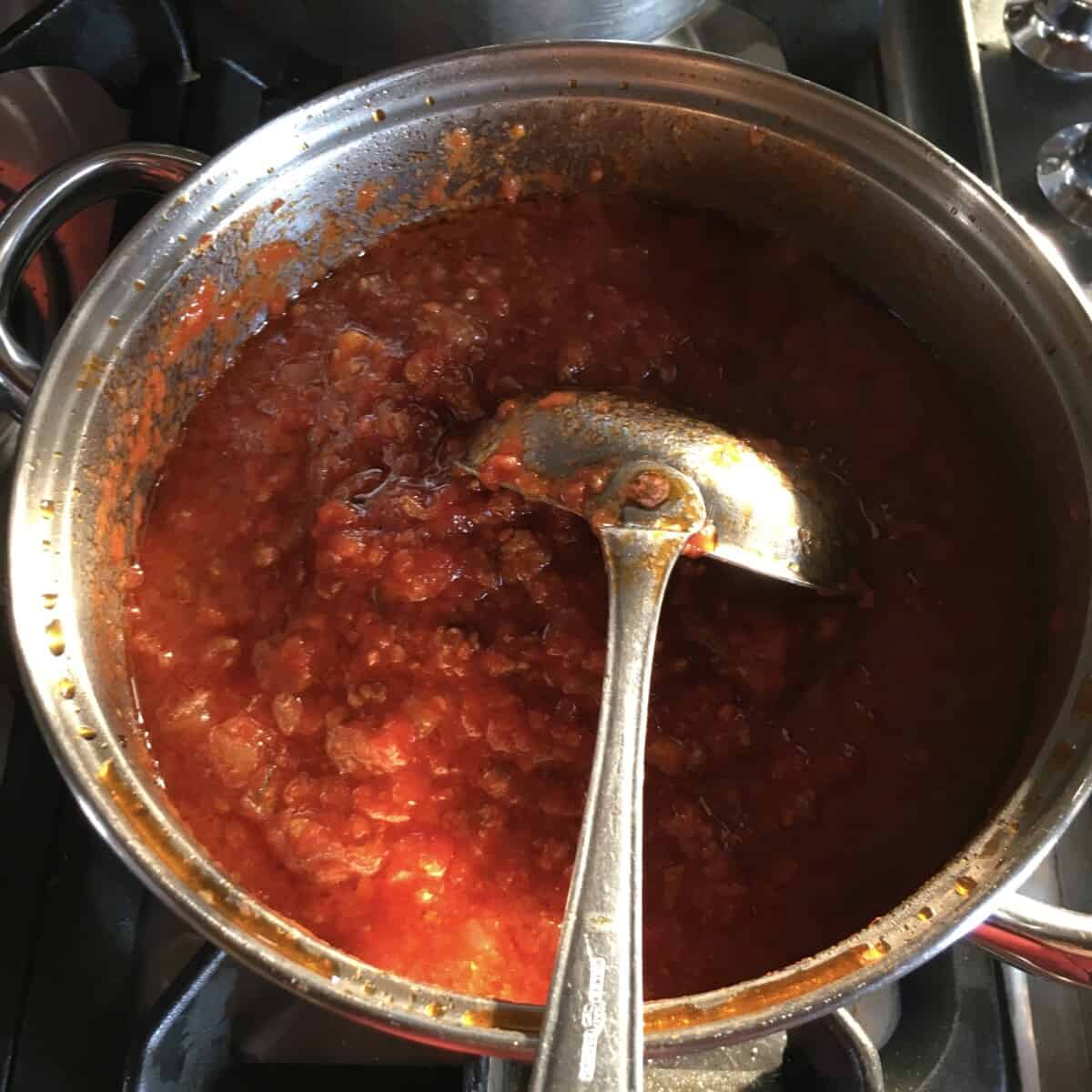 bright red italian beef ragù with a ladle turned upside down in the pot
