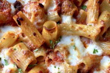 closeup of baked ziti with tomatoes and cheese covered pasta noodles some gooey and some crispy