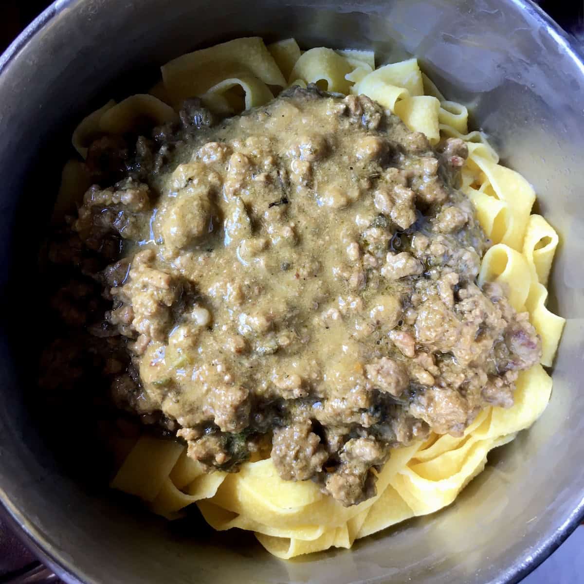 Creamy duck ragu added to cooked pappardelle pasta in a pot, homemade Italian duck ragu recipe mixed with fresh pappardelle noodles before tossing, duck ragu pappardelle preparation step.