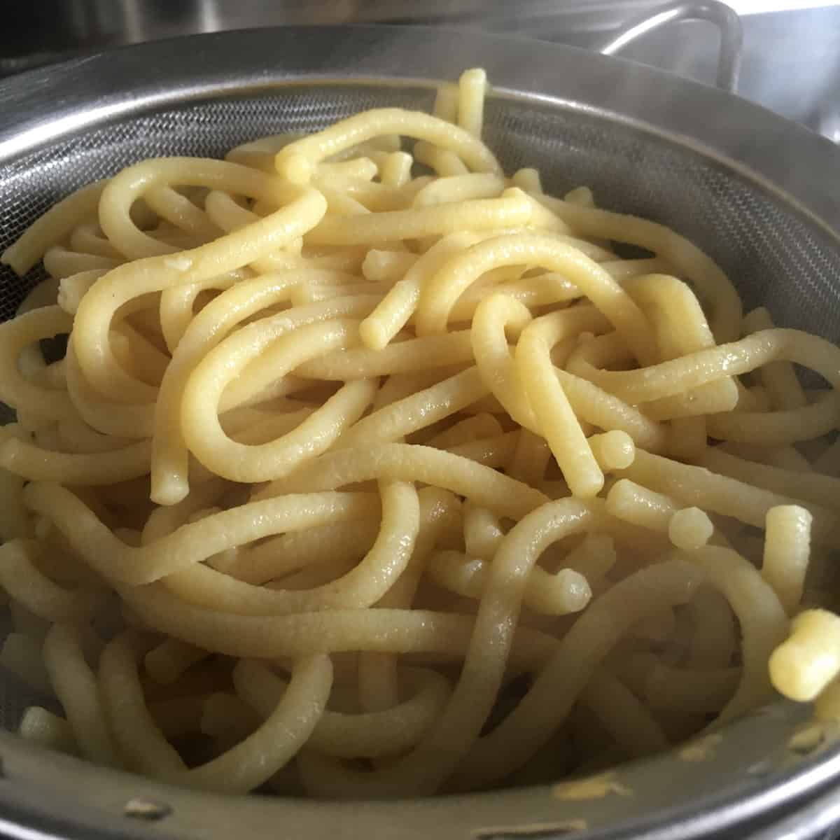 Cooked bigoli pasta in a strainer ready for duck ragu, traditional Italian bigoli noodles freshly cooked and drained, handmade bigoli pasta prepared for duck ragu recipe.
