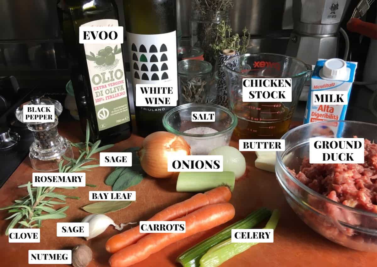 Duck ragu recipe ingredients labeled on a cutting board, fresh ingredients for making venetian duck ragu including duck meat and aromatics, Italian duck ragu preparation setup ready for cooking.